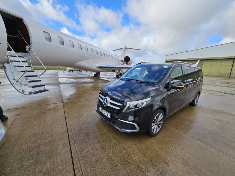 Black Mercedes V-Class waiting on the apron beside a private jet